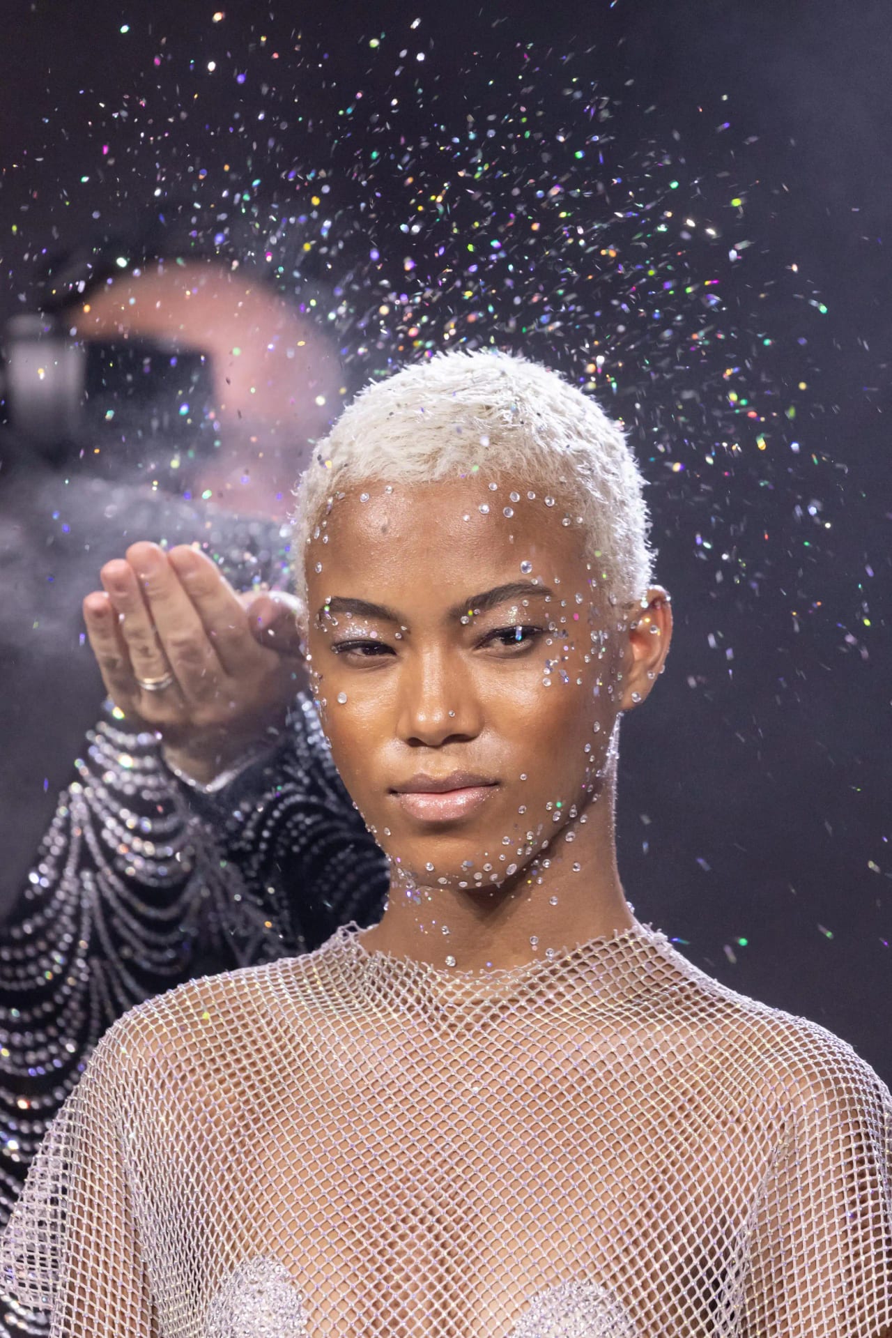 Modella sul palco con hair styling scenografico sotto le luci dello show.